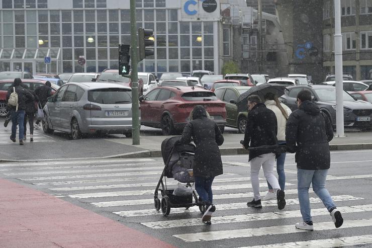 Varias persoas cruzan un paso de peóns tratando de refuxiarse da choiva na Coruña / EP