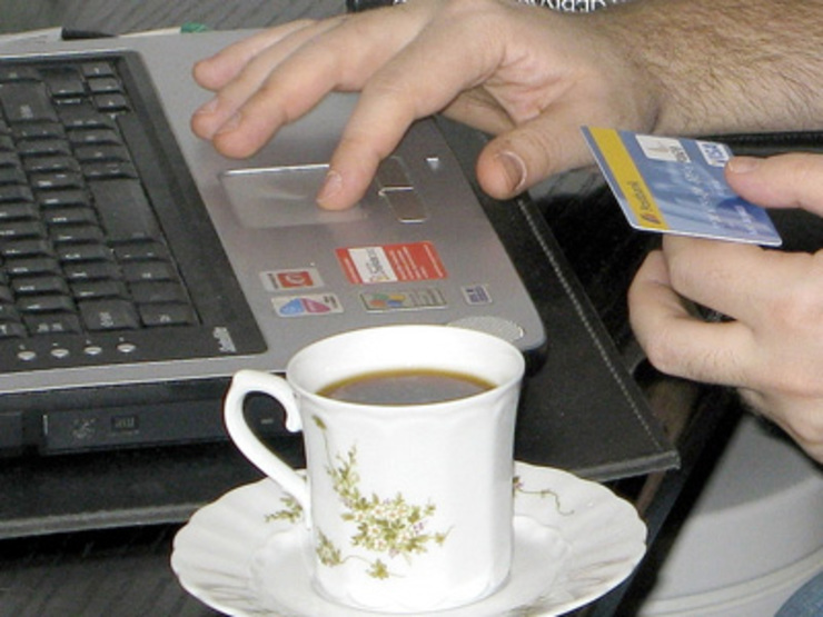 Comprando en liña mediante tarxeta de crédito e tomando un café diante do computador