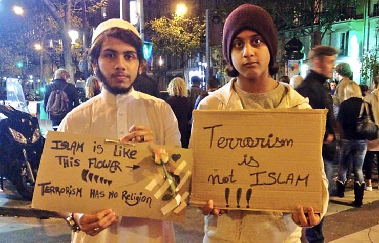 Dous mozos portan carteis para desligar o Islam do terrorismo, fronte a sala Bataclan de París, onde foron asasinadas 89 persoas na noite do 13 de novembro de 2015 / Laurie Hanna en Twitter.