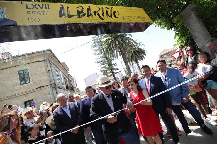 O pregoeiro da LXVII Festa do Albariño en Cambados (Pontevedra), Salvador Cores ?Manso?, xunto á alcaldesa de Cambados, Fátima Abal (con vestido vermello), corta a cinta branca para inaugurar o evento.. Beatriz Ciscar - Europa Press / Europa Press