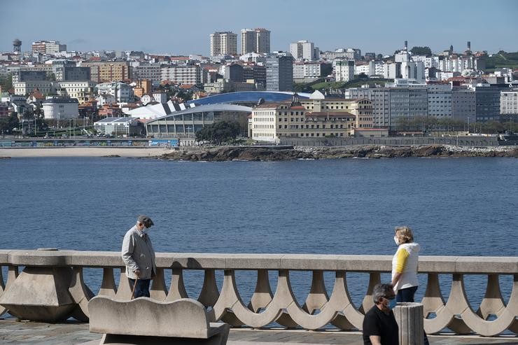 Dúas persoas pasean polo paseo marítimo da Coruña, co estadio de Riazor de fondo, a 3 de maio de 2020 