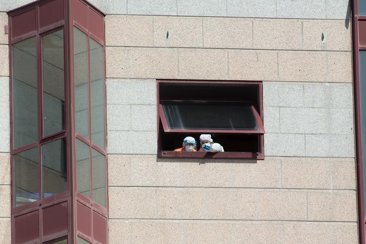Dous traballadores protexidos asómanse por unha das xanelas da residencia de maiores DomusVi de Outeiro de Rei en Lugo 