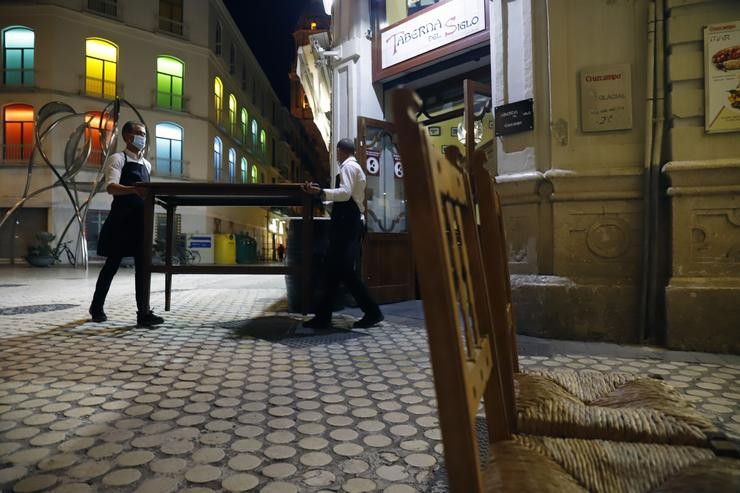 Dous camareiros afánanse en recoller a terraza do bar como consecuencia  do toque de queda imposto polo Goberno para poder frear a pandemia / Álex Zea - Europa Press.
