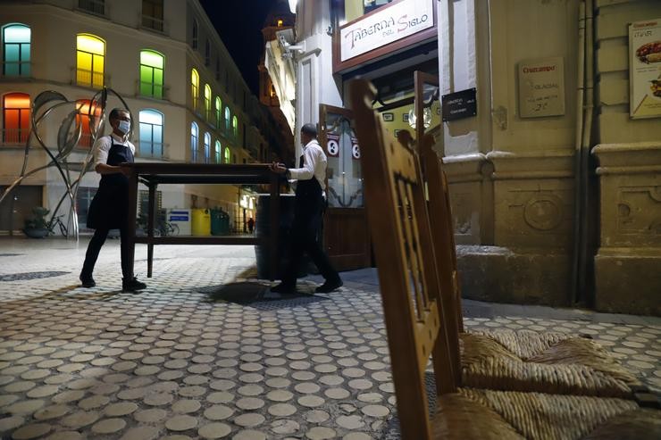 Dous camareiros afánanse en recollen a terraza do bar situado no centro da capital, como consecuencia  do toque de queda imposto polo Goberno para poder frear o contaxio en Málaga a 27 de outubro 2020. Álex Zea - Europa Press 