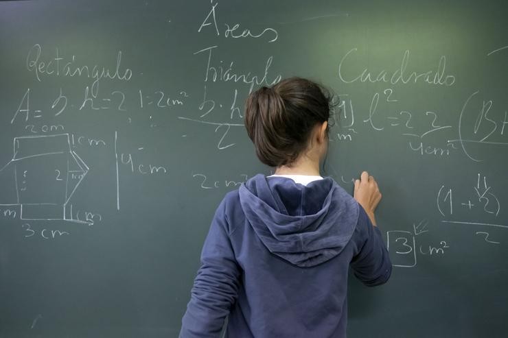 Unha estudante escribe con xiz nunha lousa nunha aula 