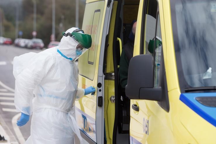 Un traballador sanitario totalmente protexido pecha a porta dunha ambulancia tras recoller a un ancián da residencia de San Cibrao 