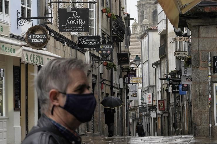Un home camiña por unha rúa con establecementos pechados durante o primeiro día de peche na hostalaría decretado debido á crise do Covid-19, en Santiago de Compostela 