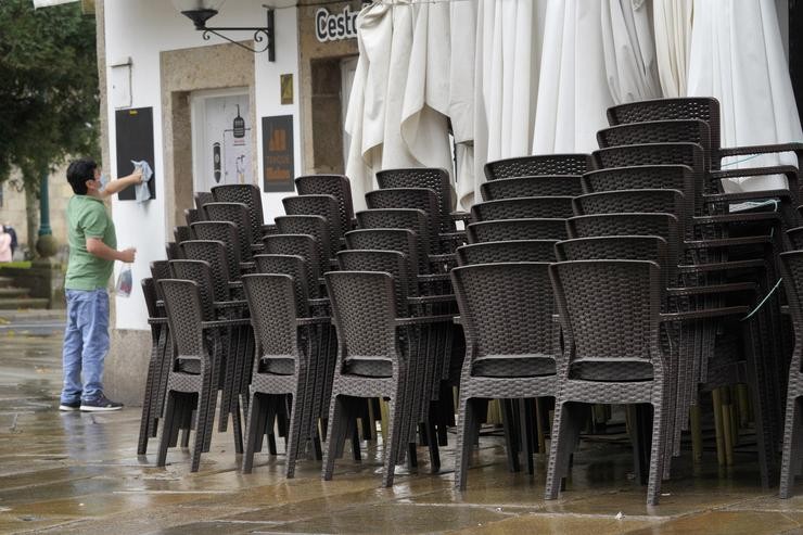 Un traballador limpa a lousa dun establecemento pechado durante o primeiro día de peche na hostalaría decretado debido á crise da Covid-19, en Santiago de Compostela 