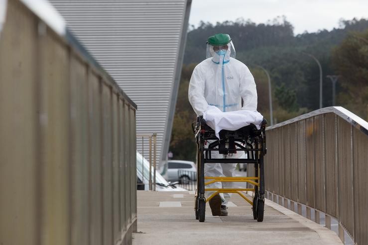 Un traballador sanitario totalmente protexido traslada unha padiola nas inmediacións dunha residencia de anciáns 