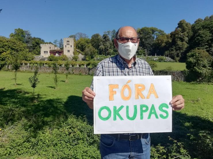 Manuel Monge cun cartel no que se le 'Fóra Okupas' e ao fondo o Pazo de Meirás 