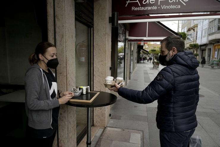 Un home recolle uns cafés dun establecemento coas novas restricións para a hostalaría 