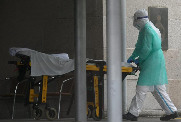 Un auxiliar de enfermería protexido contra o coronavirus transporta unha padiola desde unha ambulancia para trasladar un enfermo 