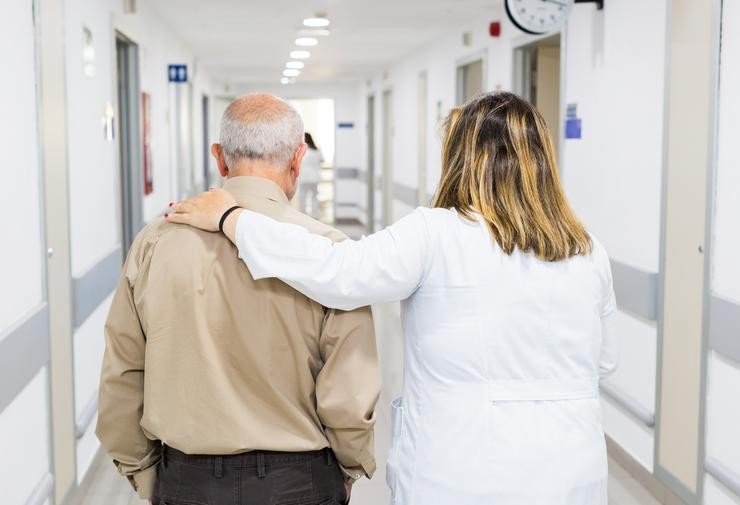 Un profesional sanitario acompaña a unha persoa maior nun hospital 