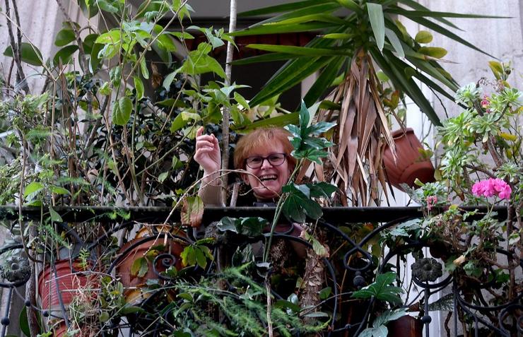 Unha muller sorrí dende o seu balcón rodeada de plantas 