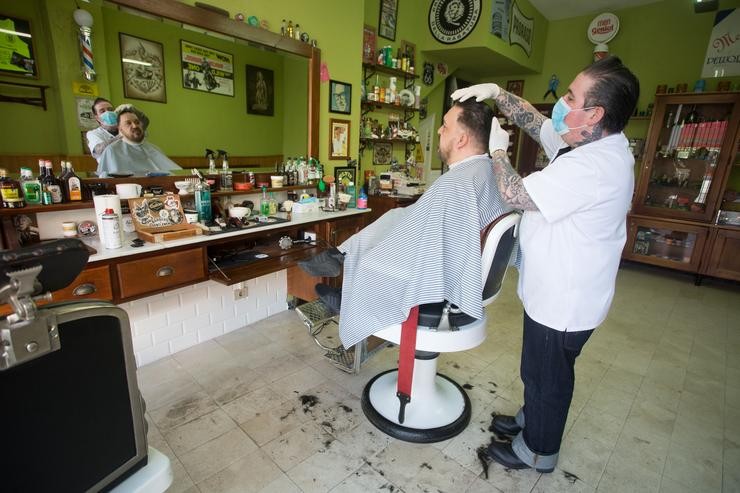 Un empregado da barbaría Rockabilly Memphis, aberta durante o día 51 do estado de alarma, peitea o pelo a un cliente 