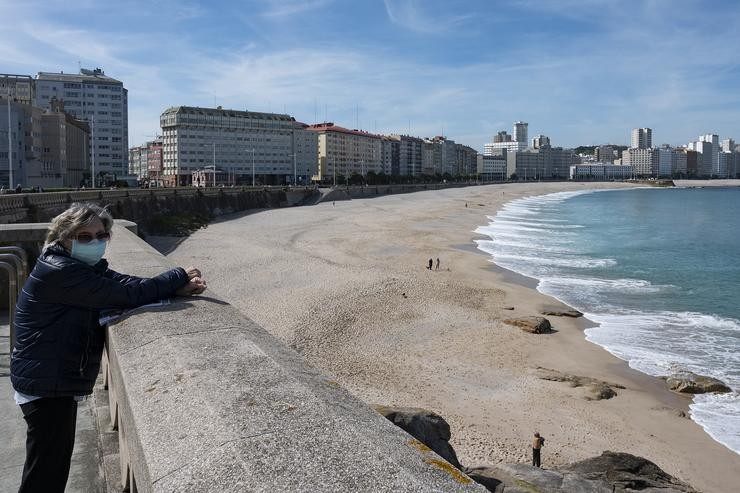 Unha muller no paseo marítimo da Coruña coa praia do Orzán de fondo 