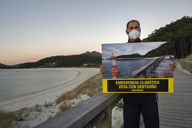 Un voluntario de Greenpeace porta unha fotografía modificada da Praia de Rodas, nas Illas Cíes, para simular os efectos da subida do nivel do mar.. GREENPEACE / Europa Press