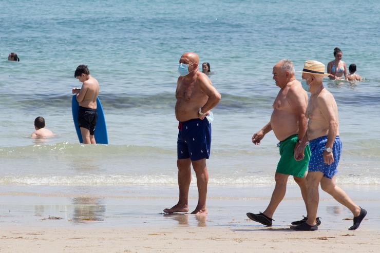 Tres homes protexidos con máscaras pasean pola Praia da Rapadoira en Foz. Carlos Castro - Europa Press