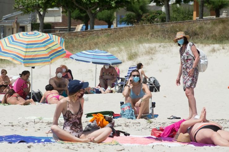 Varias persoas protexidas con máscaras toman o sol na Praia da Rapadoira en Foz 