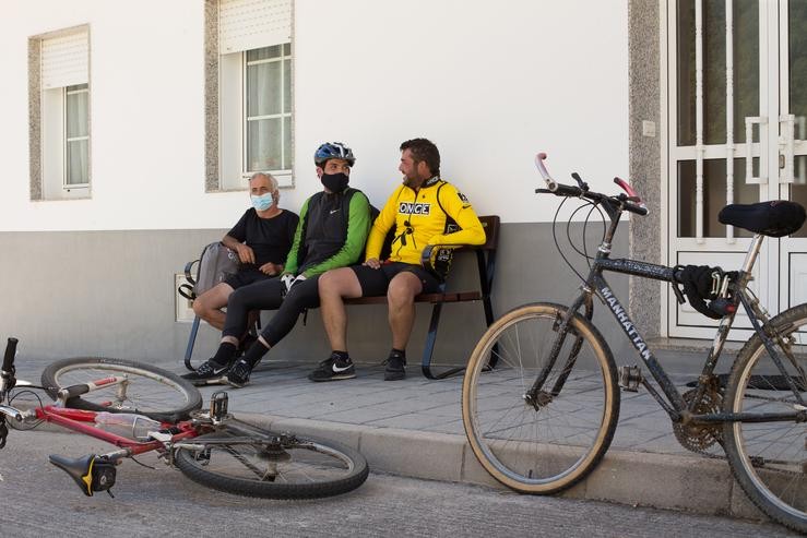 Os irmáns Primi (d) e Mario (c) e o seu tío Pedro (i), descansan xunto ás súas bicicletas nun banco da localidade de Triacastela, fin da súa etapa diaria, mentres os peregrinos retornan ao Camiño francés da Ruta Xacobea  