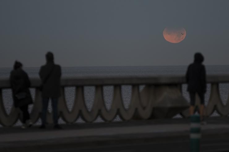 Tres persoas observan a eclipse lunar parcial desde A Coruña, a 19 de novembro de 2021, na Coruña, Galicia, (España).. M. Dylan - Europa Press / Europa Press