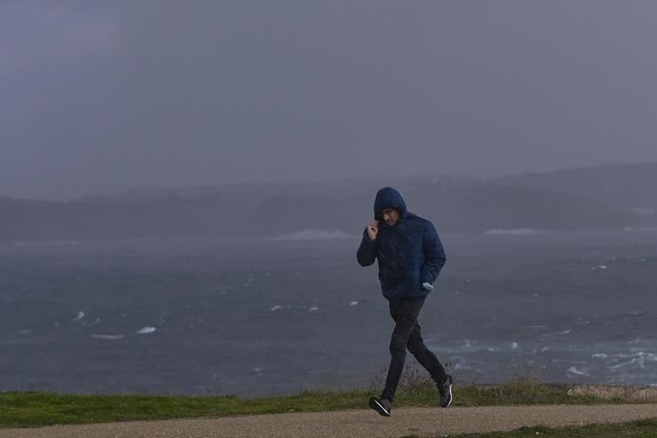 Un home protéxese do vento e a choiva na zona da Torre de Hércules. M. Dylan - Europa Press
