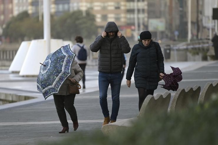 Tres persoas con paraugas no Paseo Marítimo da Coruña onde se aprecia forte vento como consecuencia da borrasca Varra, a 7 de decembro de 2021 / M. Dylan - Europa Press.