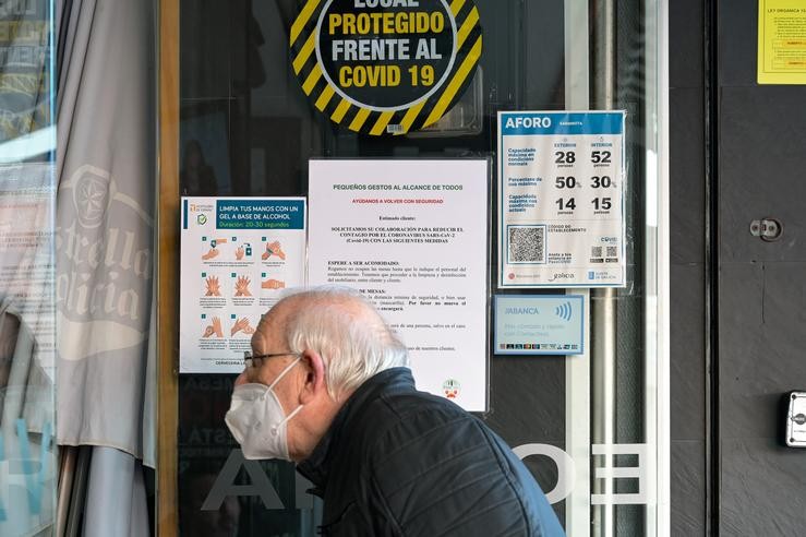 Un home pasa fronte a carteis onde se mostra a cacidade e o código QR na porta dun restaurante na Coruña 