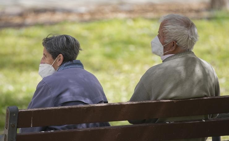 Un home e unha muller maiores, sentados nun banco e con máscara contra a covid-19, nun parque 
