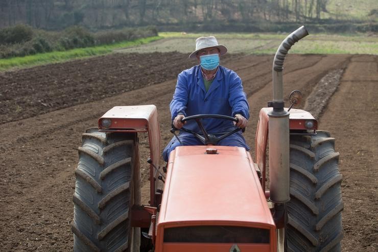 Manuel Rodríguez ara as súas leiras co tractor e máscara para plantar patacas en Lugo, a 24 de marzo de 2021. O sector primario foi fundamental durante a pandemia de covid-19 / Carlos Castro - Europa Press.