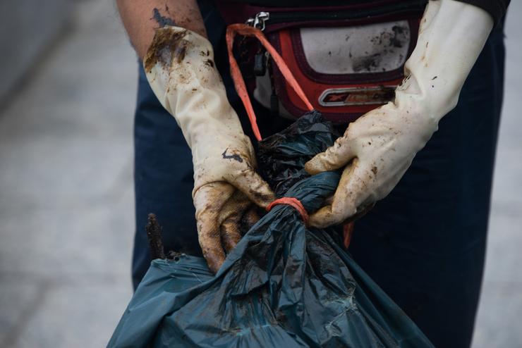 Unha muller pecha unha bolsa cos restos de chapapote mesturados con algas recollidos nunha praia da Illa de Arousa, a 13 de decembro de 2022, en Illa de Arousa, Pontevedra, Galicia (España). Polo momento descoñécese a orixe da vertedura de chapapo. Gustavo da Paz - Europa Press 