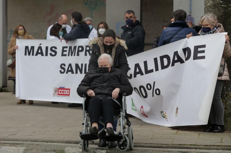 Unha muller en cadeira de rodas pasa por diante de varios sanitarios que protestan, cunha pancarta que reza 