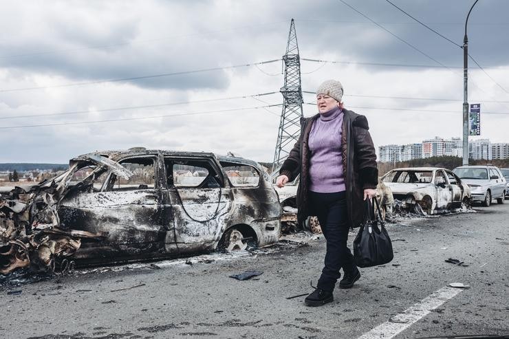 Unha muller camiña diante duns coches queimados nunha ponte de Irpin, a 7 de marzo de 2022, en Ucraína. O exército de Ucraína resiste polo momento o duro asedio de Rusia 