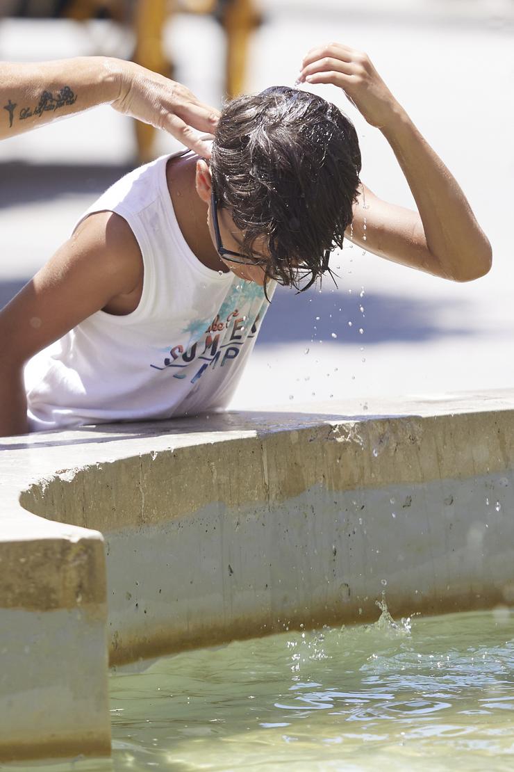Un neno bota auga pola cabeza para refrescarse durante unha onda de calor / Joaquin Corchero - Europa Press
