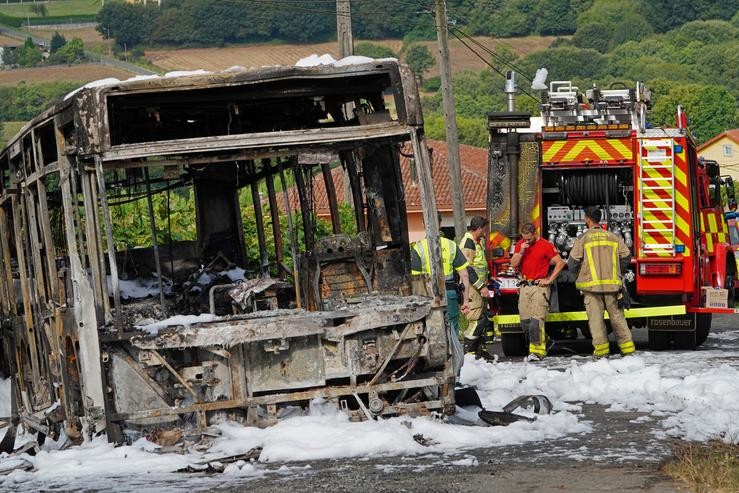 O autobús calcinado xunto a varios bombeiros durante o dispositivo de extinción do incendio, onde faleceu un bombeiro en prácticas, 