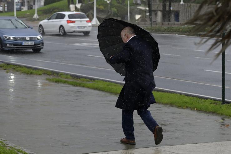 Un home con paraugas trata de refuxiarse do vento e da choiva, a 4 de novembro de 2023, na Coruña 
