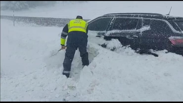 Un Garda Civil quitando neve dun coche atrapado na montaña de Lugo