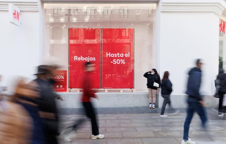 Varias persoas camiñan fronte a unha tenda de H&M co cartel de rebaixas 