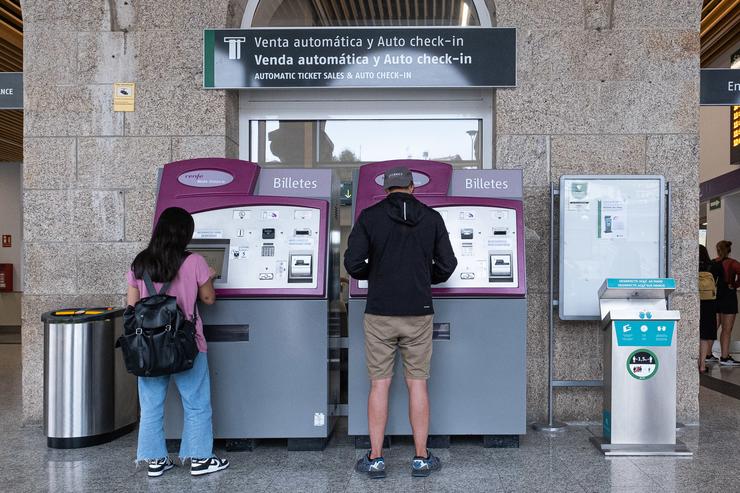 Dúas persoas compran billetes nos caixeiros de venda automática na estación de trens de Santiago de Compostela 