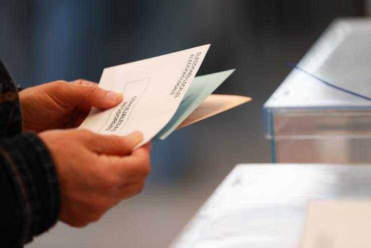 Unha persoa sostén papeletas electorais fronte ás urnas / Tomàs Moyà - Arquivo