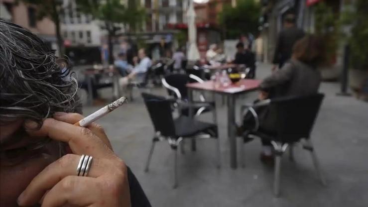 Mujer fumando en una terraza, con fumadores pasivos a su espalda / EFE - Arquivo