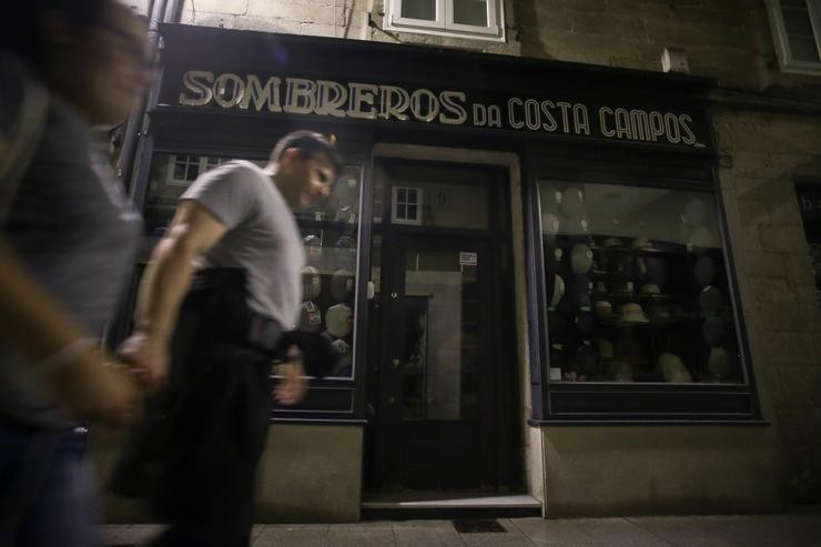 Varias persoas camiñan á beira dunha tenda de roupa sen iluminación 