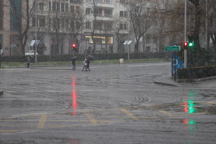 Varias persoas cruzan unha rúa durante unha treboada, no centro de Madrid 