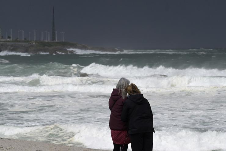 Dúas mulleres observan as ondas durante a fronte meteorolóxica, a 23 de febreiro de 2024, na Coruña, Galicia (España). A Axencia Estatal de Meteoroloxía (Aemet) decretou un aviso laranxa por temporal costeiro no litoral galego que xa está activo. O non. M. Dylan - Europa Press 