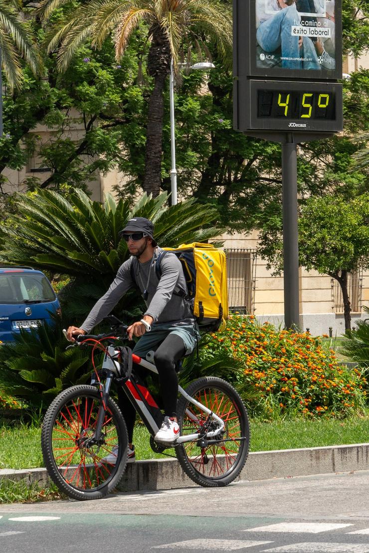 Un termómetro marca 45 graos ás 14:00 da tarde xunto a un traballador de Glovo en bicicleta, a 19 de xullo de 2024, en Sevilla, Andalucía.. Francisco J. Olmo - Europa Press 