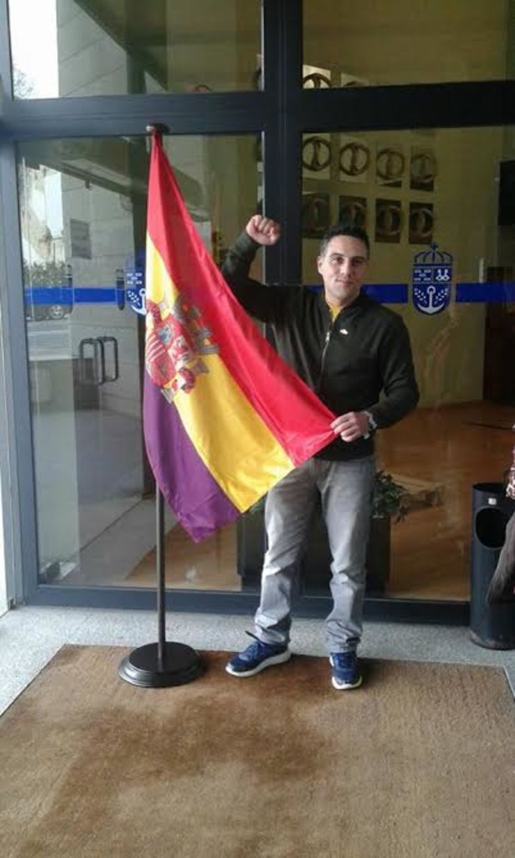 O concelleiro de EU en Narón, André Abeledo, cunha bandeira republicana diante da porta deste concello