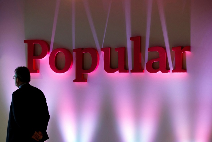 FILE PHOTO: A man casetas next to the logo of Spain's Banco Popular during the b