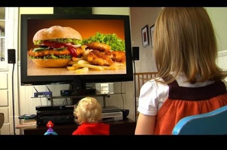 Cativos ven na televisión un anuncio de hamburguesas.