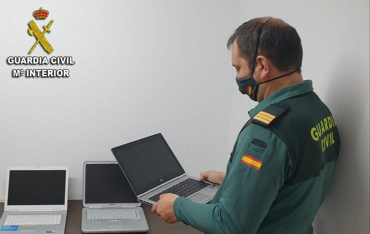 Un garda civil toma un dos computadores portátiles. GARDA CIVIL
