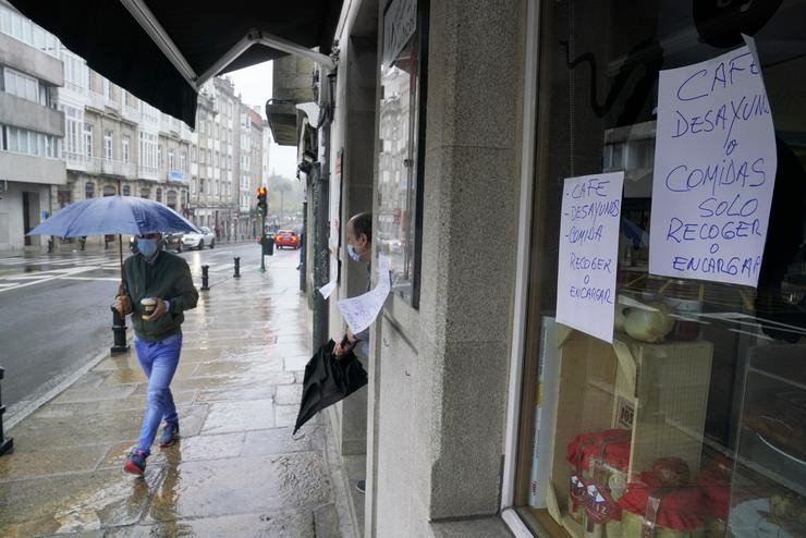 Un home pasa á beira dun establecemento pechado onde se pode ler 'Café, almorzos, ou comidas, só recoller ou encargar'  durante o primeiro día de peche na hostalaría decretado debido á crise do Covid-19, en Santiago de Compostela, Galicia,. Álvaro Ballesteros - Europa Press 